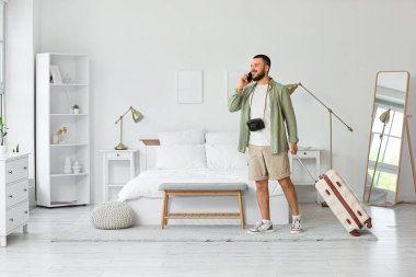 Otel odasında çantalı bir erkek turist cep telefonuyla konuşuyor.