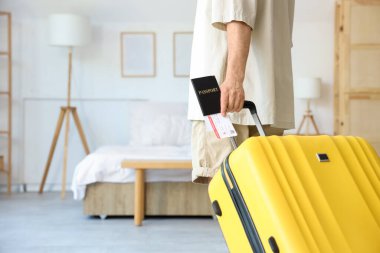 Otel odasında pasaport ve bavul taşıyan erkek turist.