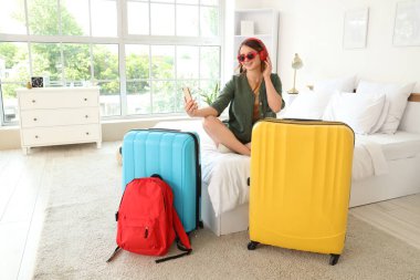 Kulaklıklı ve çantalı kadın turist otel odasında selfie çekiyor.