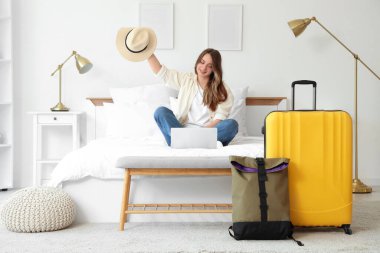 Şapkalı ve dizüstü bilgisayarlı kadın turist otel odasında sohbet ediyor.