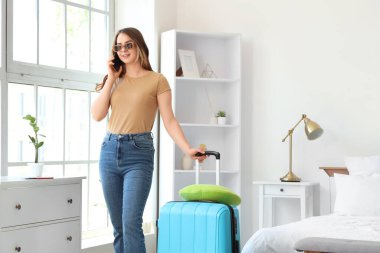 Otel odasında çantalı bir kadın turist cep telefonuyla konuşuyor.
