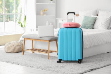 Otel odasında halının üzerinde boyun yastığı olan bavul.