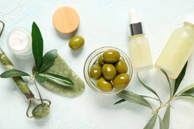 Doğal kozmetik ürünleri, yüz masajı aletleri ve açık arkaplanda yeşil zeytinli kompozisyon