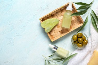 Doğal yağ şişeleri, guasha masaj aleti ve açık arkaplanda yeşil zeytinlerle kompozisyon