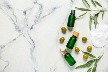 Doğal esanslı yağ, pamuk pedleri ve hafif arkaplanda yeşil zeytinlerle kompozisyon