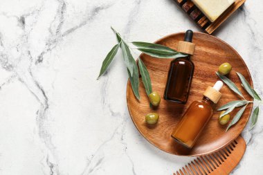 Doğal yağ, sabun, saç tarağı ve açık arkaplanda yeşil zeytin şişeleriyle kompozisyon