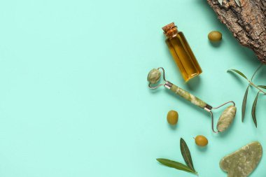 Doğal yağ şişesi, yüz masajı aletleri ve arka planda yeşil zeytinlerle kompozisyon