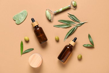 Doğal kozmetik ürünleri, yüz masajı araçları ve arka planda yeşil zeytinli kompozisyon