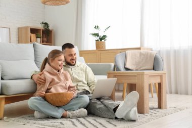 Mutlu baba ve kızı evde dizüstü bilgisayar izliyorlar.