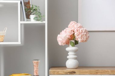 Odadaki rafta pembe ortanca çiçekleri olan vazo.