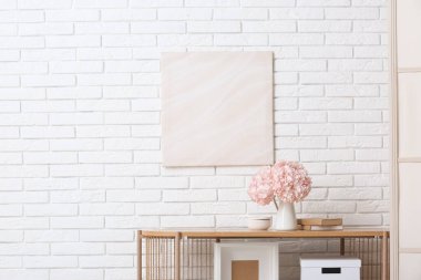 İçinde pembe ortanca çiçekleri ve kitapların bulunduğu vazo beyaz tuğla duvarın yanındaki odada.