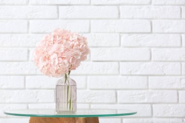 Beyaz tuğla duvarın yanındaki masada pembe ortanca çiçekli vazo.