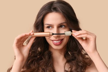 Beautiful young woman with mascara on brown background