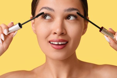 Güzel genç Asyalı kadın sarı arka plana rimel sürüyor, yakın plan.