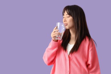 Genç Asyalı kadın leylak arka planda su içiyor.