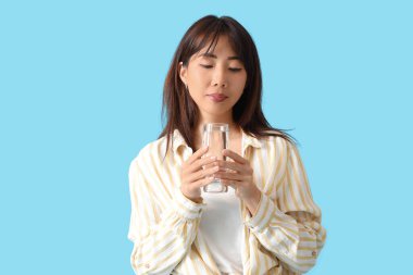 Mavi arka planda bir bardak su olan genç Asyalı kadın.