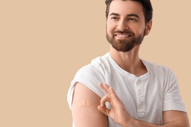 Uygulamalı tıbbi yaması olan genç adam bej arka plandaki aşıdan sonra iyi görünüyor.