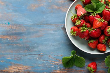 Mavi ahşap arka planda olgun çilek tabağı.