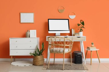 Modern bilgisayar, ev bitkileri ve turuncu duvarın yanındaki çekmecelerle rahat çalışma alanı