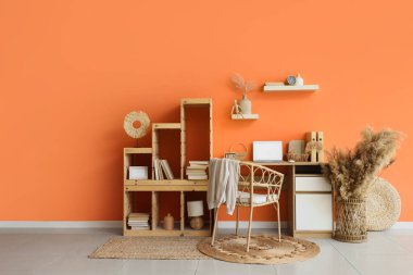 Modern dizüstü bilgisayar, klasörler ve turuncu duvarın yanındaki raf ünitesi ile rahat çalışma alanı