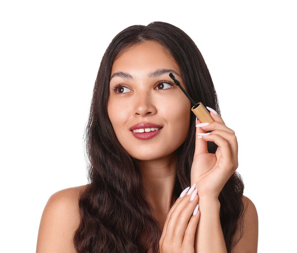 Красивая молодая азиатка наносит тушь на белый фон