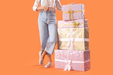 Turuncu arka plandaki hediye kutularını gösteren olgun bir kadın.