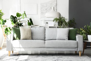 Rahat gri kanepe ve çiçeklerle aydınlık oturma odasının içinde.