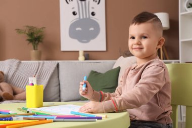 Masada keçeli kalemlerle çizen komik küçük çocuk.