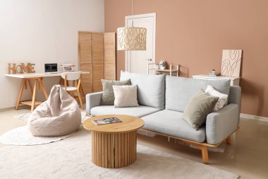 Gri kanepesi, fasulye koltuğu ve bej duvarın yanındaki ahşap sehpası olan şık bir oturma odası.