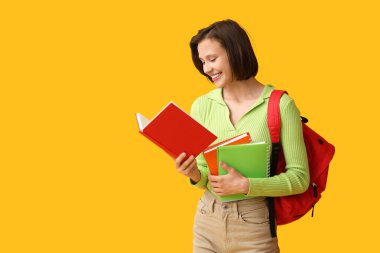 Sırt çantası ve sarı arka planda defterleri olan güzel bir kız öğrenci.