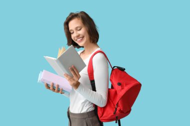 Mavi arka planda kitapları ve sırt çantası olan güzel bir kız öğrenci.