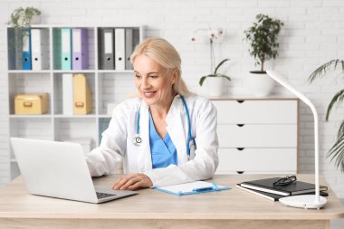 Klinikte masada dizüstü bilgisayarla çalışan kadın doktor