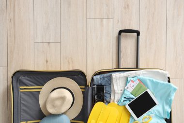 İçinde giysiler, plaj aksesuarları, pasaport, tablet ve kamera olan bavulu oturma odasında aç.