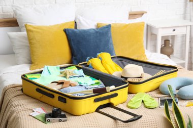 Yatak odasında üzerinde giysiler, plaj aksesuarları, dürbün ve kamera olan bavulu aç.