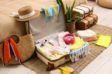 İçinde giysiler, plaj aksesuarları, kulaklıklar, cep telefonu ve pasaport bulunan bavulları yatak odasının yanında yere yakın.