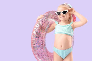 Mor arka planda şişirilebilir yüzüğü olan, mayo ve güneş gözlüğü takan şirin, mutlu bir kız.