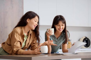 Mutlu genç bayan en iyi arkadaşlar ellerinde kahve fincanlarıyla mutfakta dergi okuyorlar.