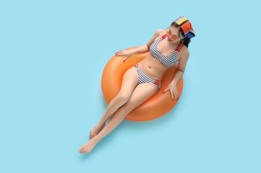 Mavi arka planda uzanan, çizgili mayolu, şişme yüzüklü güzel bir kadın.