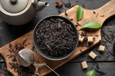 Siyah çay yapraklı kase ve siyah ahşap arka planda çaydanlık.