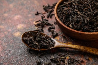 Koyu arka planda kuru siyah çay yaprakları olan tahta kaşık ve kase, yakın plan.