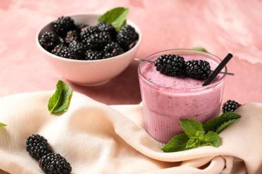 Bir bardak taze böğürtlenli, naneli ve pembe arkaplanlı meyve püresi.