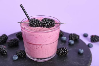 Bir bardak taze böğürtlen suyu ve leylak arkaplanda yaban mersini.