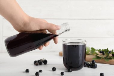 Kadın beyaz ahşap arka planda şişeden cama taze kuş üzümü suyu döküyor.