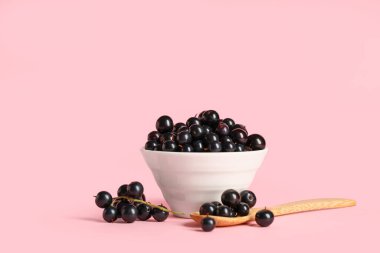 Pembe arka planda taze siyah üzümlü kase ve tahta kaşık.