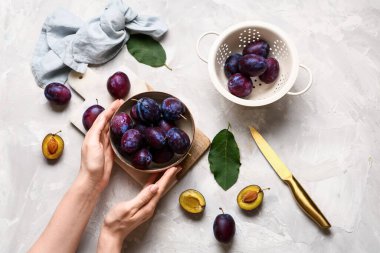 Kaseli kadın elleri ve gri arka planda taze olgun erikler.