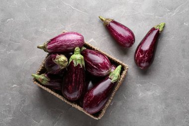 Gri arka planda taze olgun patlıcanlarla dolu bir hasır kutu.