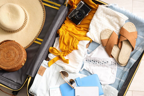 Open suitcase with clothes, beach accessories and camera on floor in living room, top view
