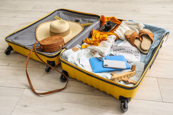 Открытый чемодан с одеждой, пляжными принадлежностями, мобильным телефоном и фотоаппаратом на полу в гостиной