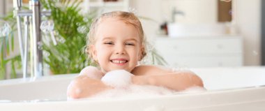 Tatlı küçük kız köpükle banyo yapıyor ve sabun köpüğü banyoda banyo yapıyor.