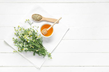 Bir kase bal, taze ve kurumuş papatya çiçekleri açık ahşap arka planda